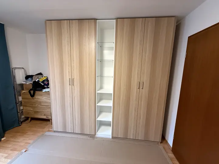 Kleiderschrank in Holzoptik mit Drehtüren und offenem weißen Mittelregal.