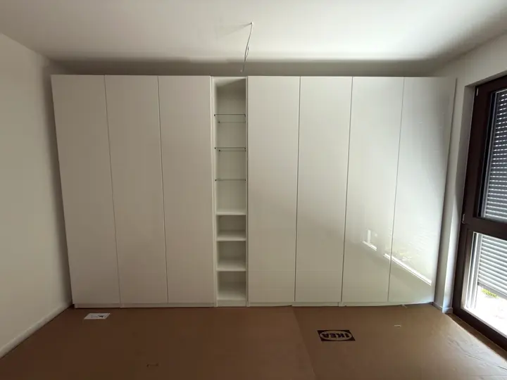 Weißer PAX Kleiderschrank mit offenem Regalfach.