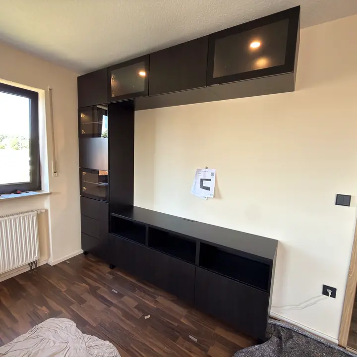 Montierte schwarze Wohnwand mit Hochschrank, Hängeschränken und TV-Lowboard.